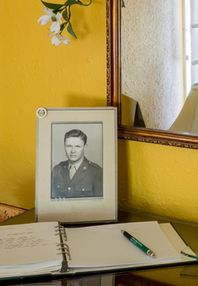 Framed picture of man in uniform, gold walls with mirror, guestbook with green pen.