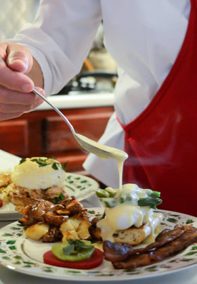 Person with red apron holdingspoon with cheese sauce drizzling over rolled omelet on holly desinged plate.