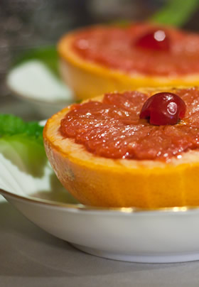 Cream bowls with gold trim with grapefruit cut in half, cherry on top.