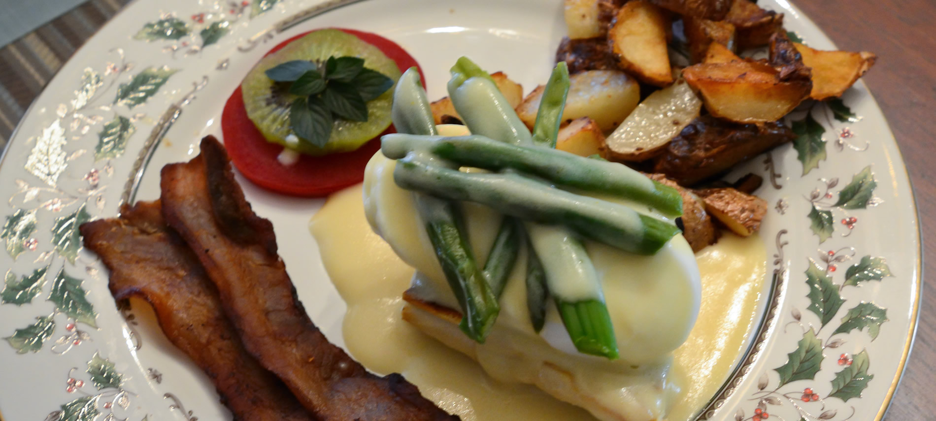 Cream plate with holly design, bacon, fried potatoes, hard-boiled egg with asparagus and cream sauce.