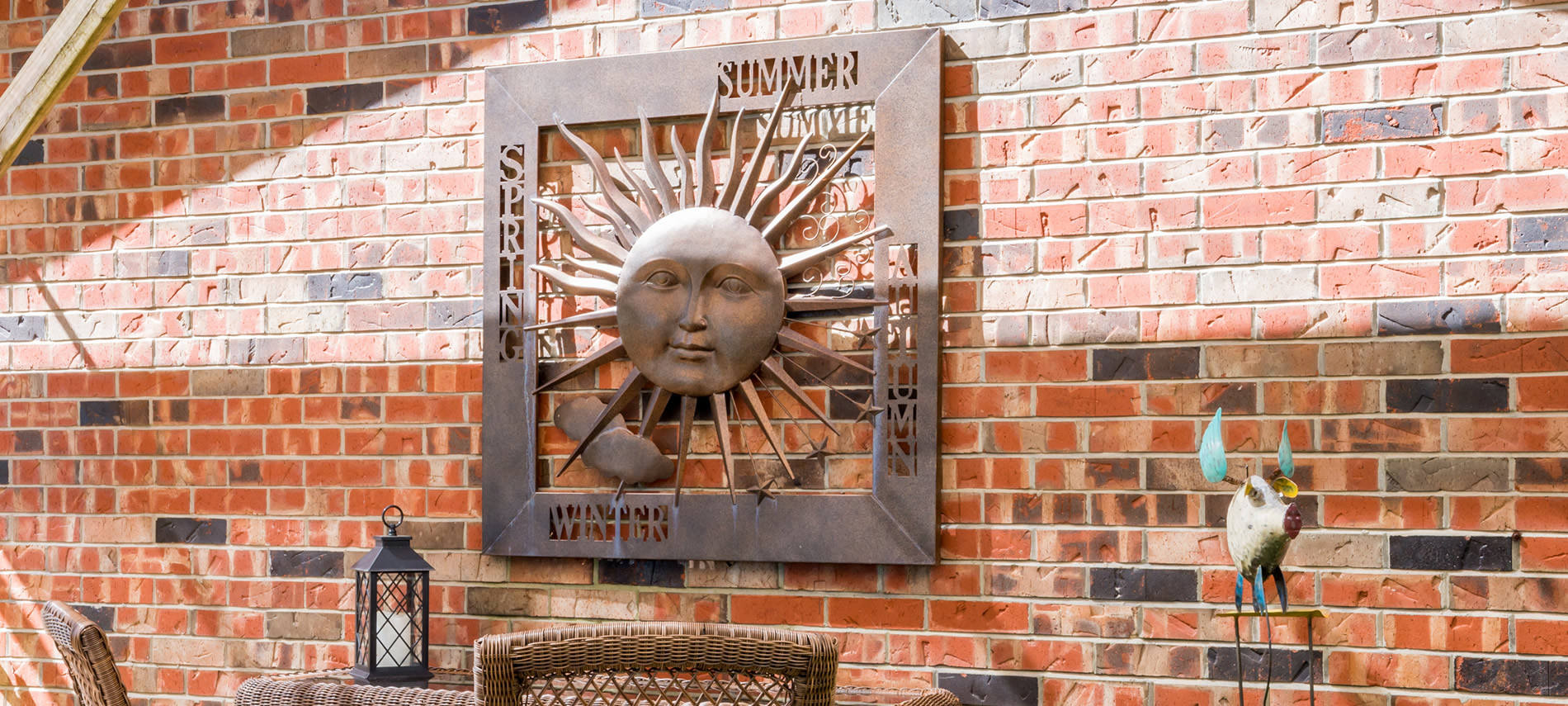 Red brick wall with metal sun hanging listing 4 seasons, wicker chairtops.